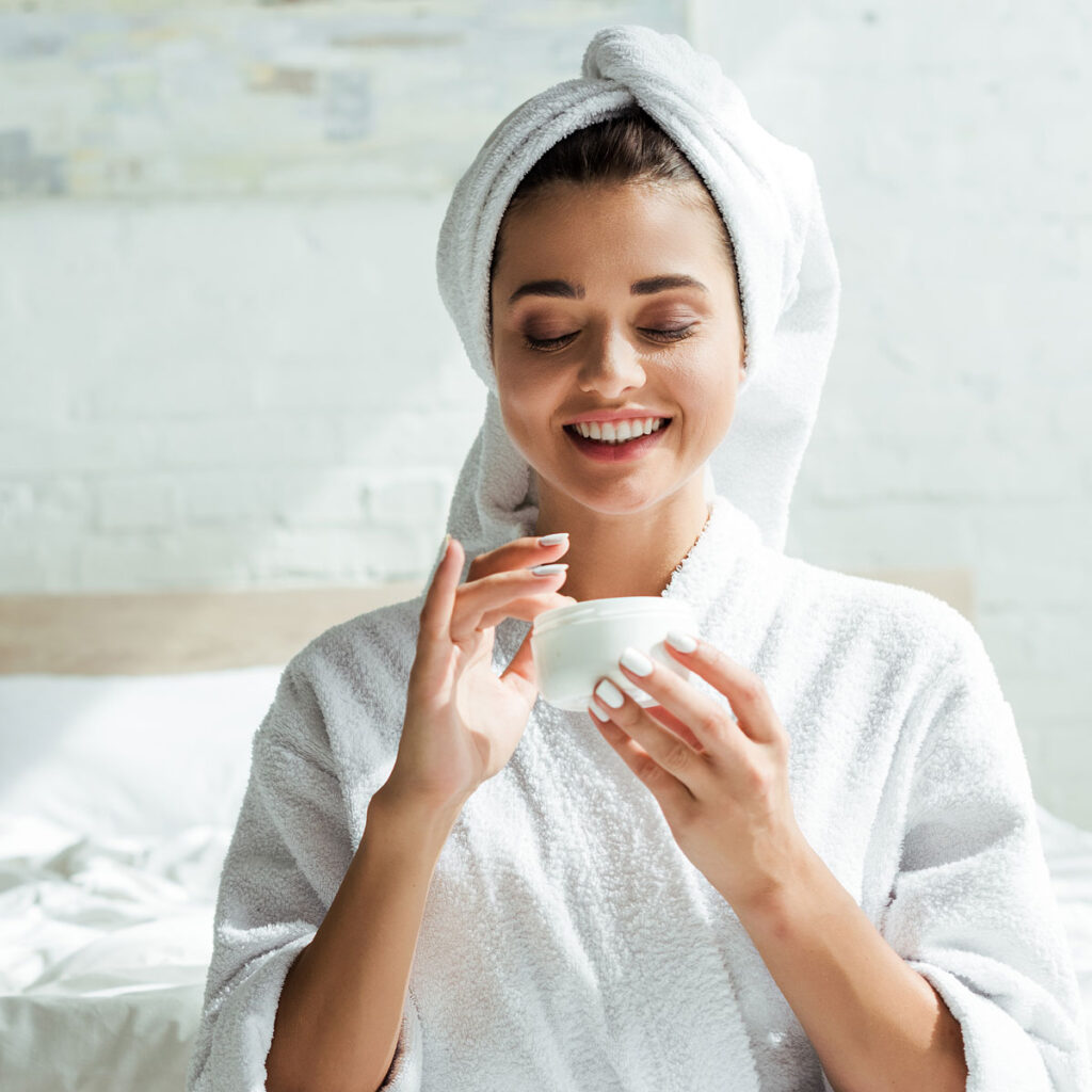 Eine Frau im Bademantel und einem Handtuch-Turban freut sich über eine Creme