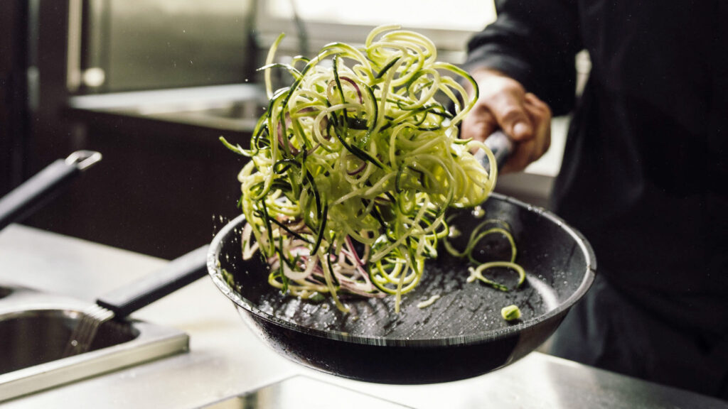 Aufnahme von Koch wie er Zucchini-Nuddeln in der Pfanne schwenkt.