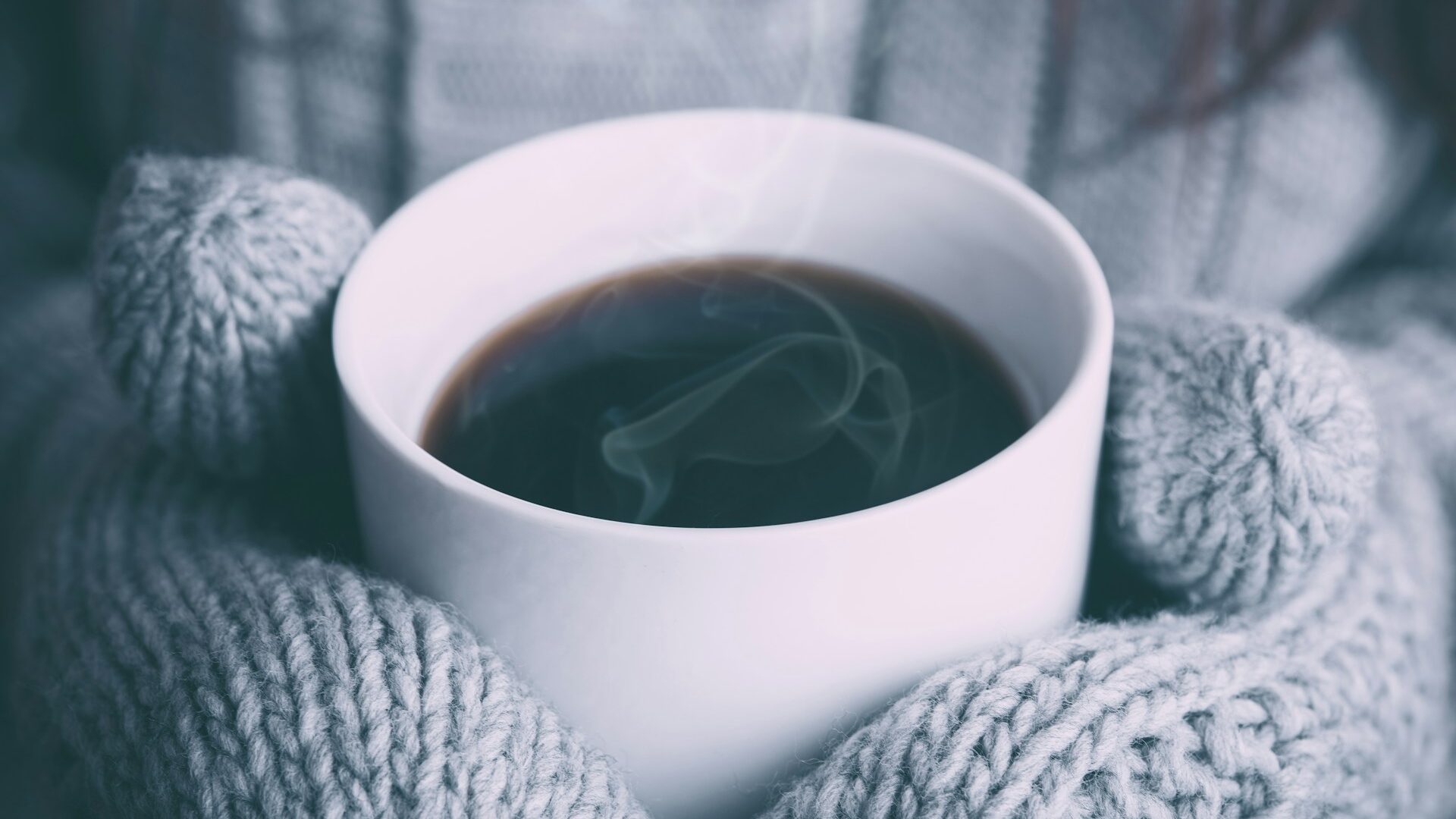 Aufnahme einer Kaffeetasse die von Handschuhen gehalten wird.